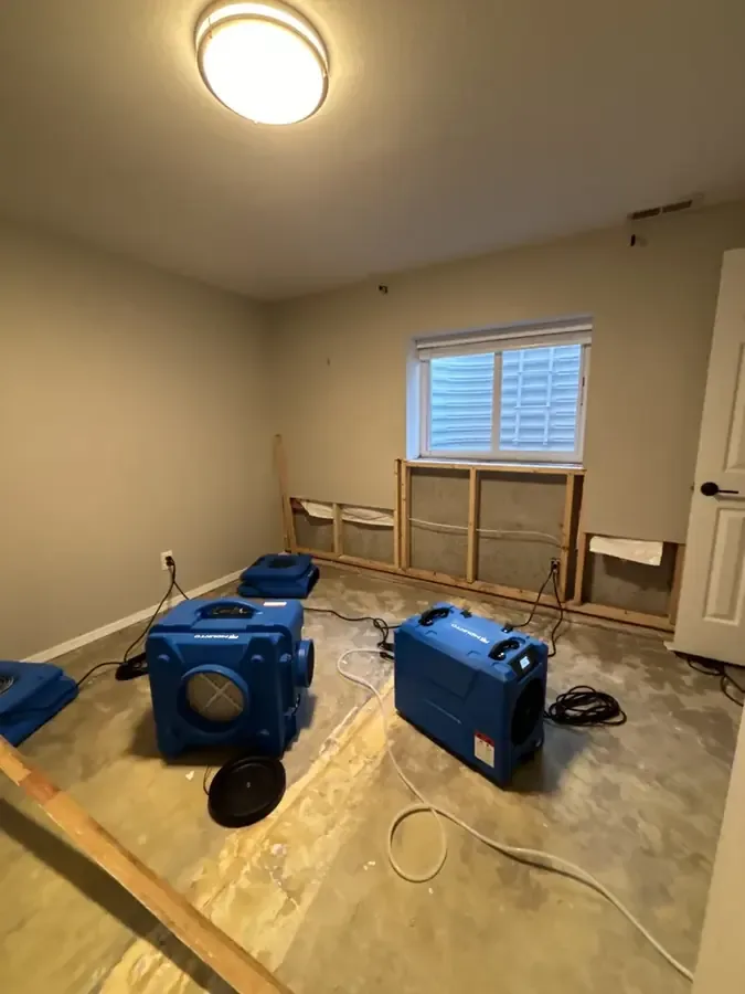 Air movers stand in a room undergoing drying after a water leak.