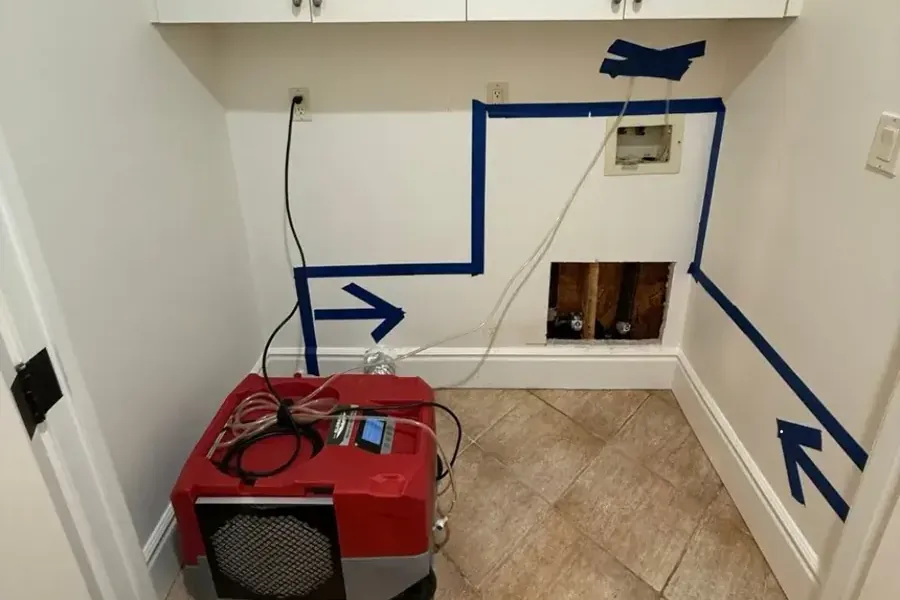 Blue tape marks a wet wall area above a dehumidifier and an opened wall section