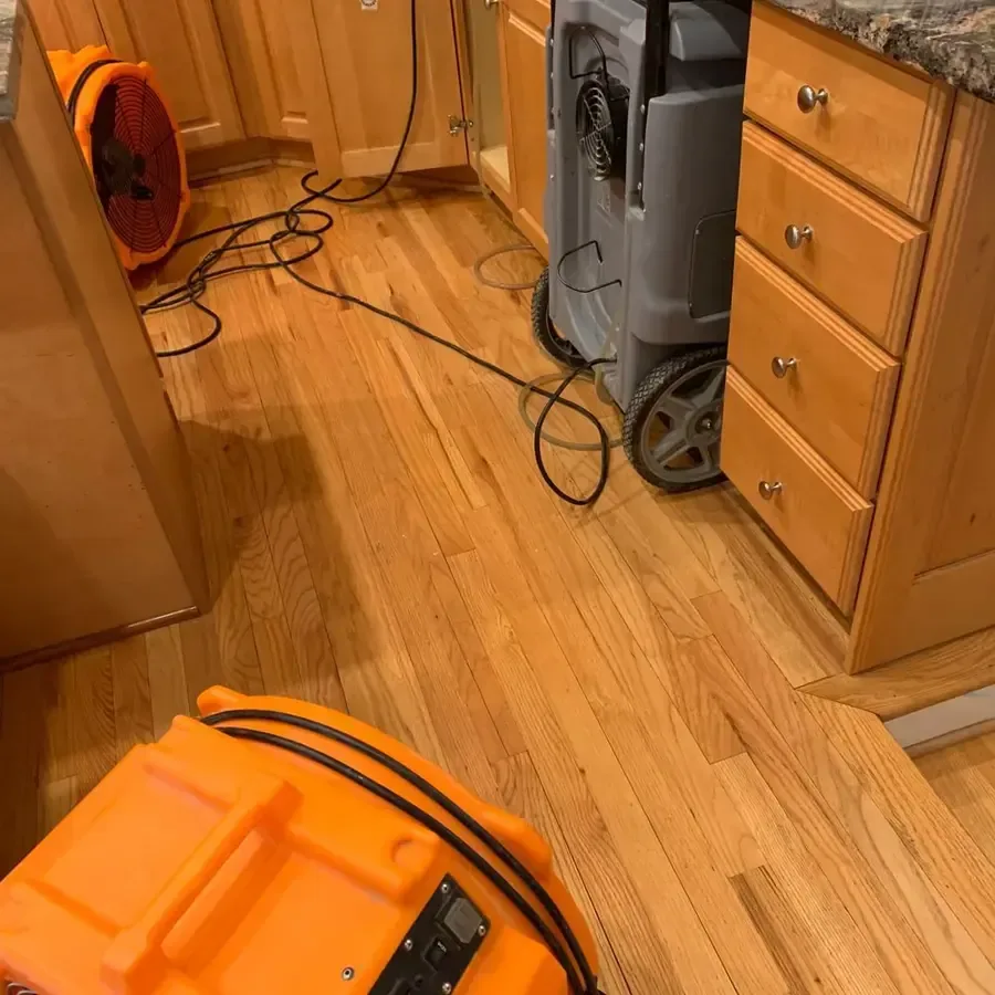 An air mover and dehumidifier dry a hardwood kitchen floor after water damage.