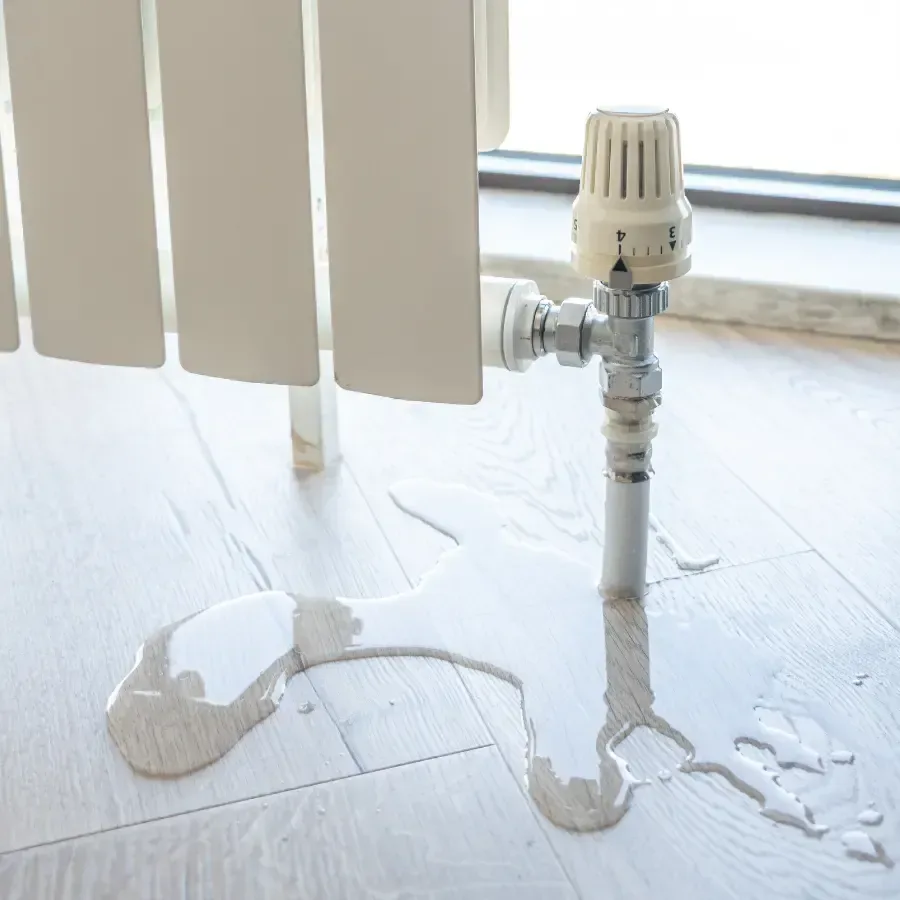 Water leaking from a radiator and spreading across the light colored floor underneath it