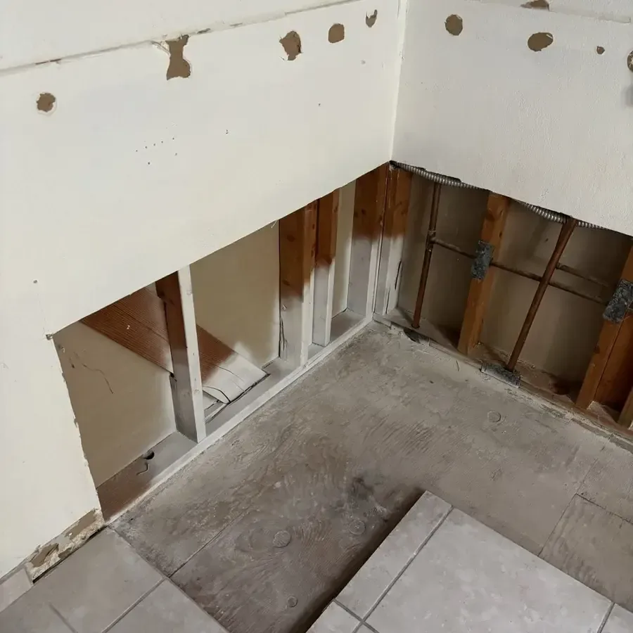 An opened wall cavity above a tiled floor exposes framing for drying after a leak