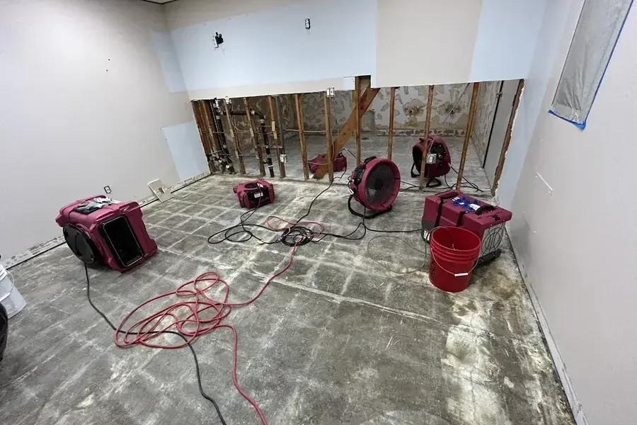 Air movers and dehumidifiers arranged across an exposed slab beside an opened lower wall