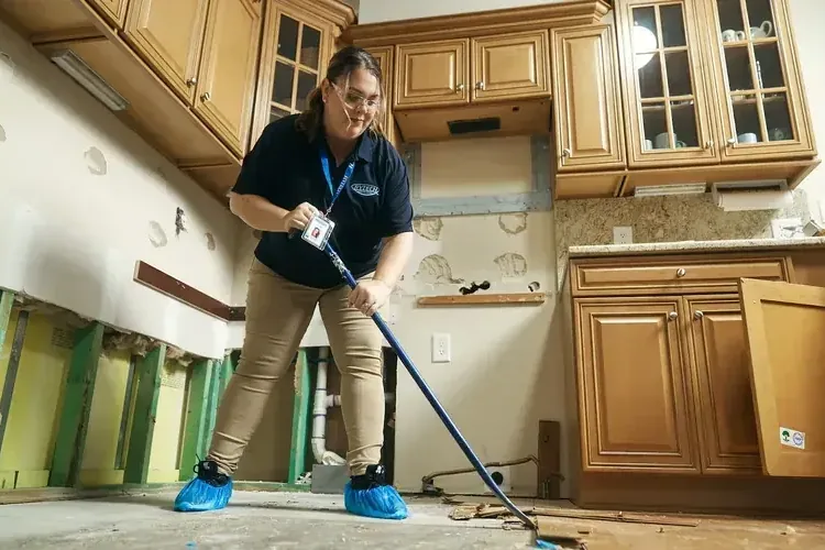 Technician using an extraction wand on a kitchen floor beside opened cabinet bases